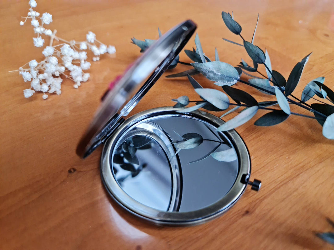 Compact mirror on a wooden surface with decorative plants