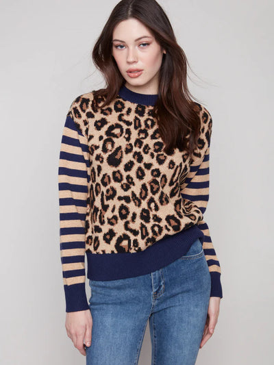 Woman wearing a leopard print sweater with blue stripes and jeans on a plain background