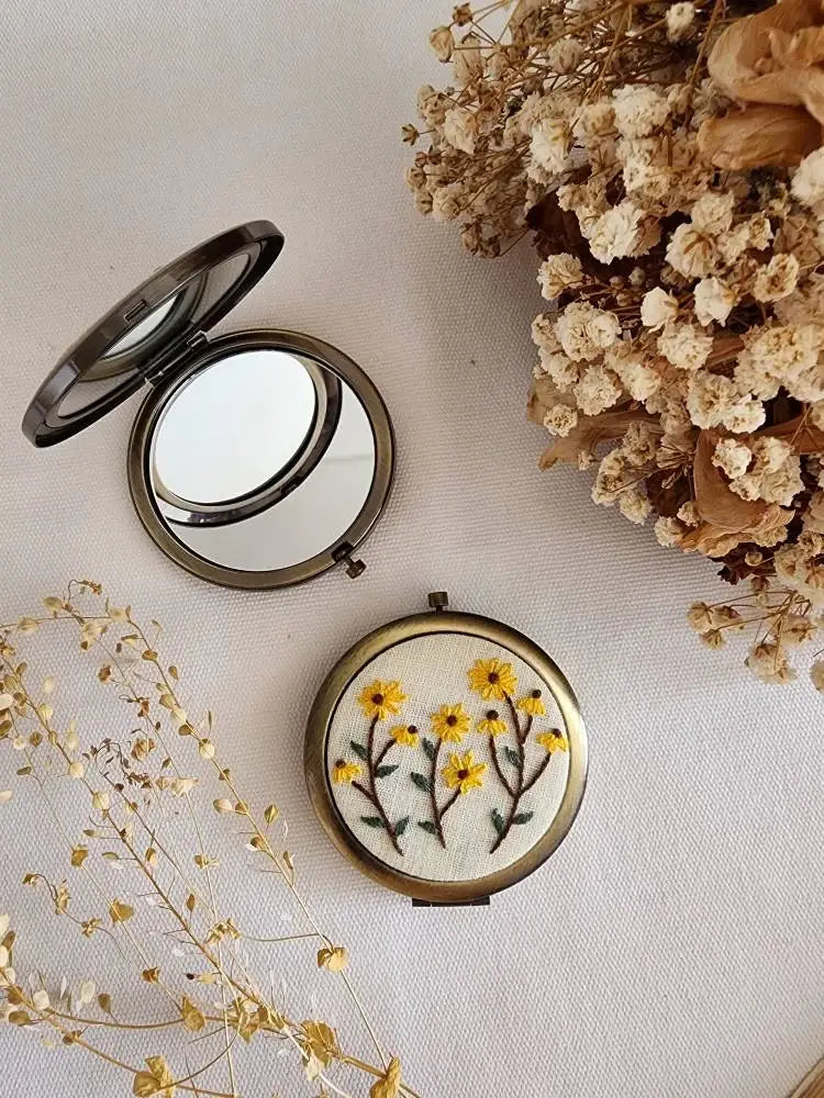 Compact mirror with floral design on a light background with dried flowers.