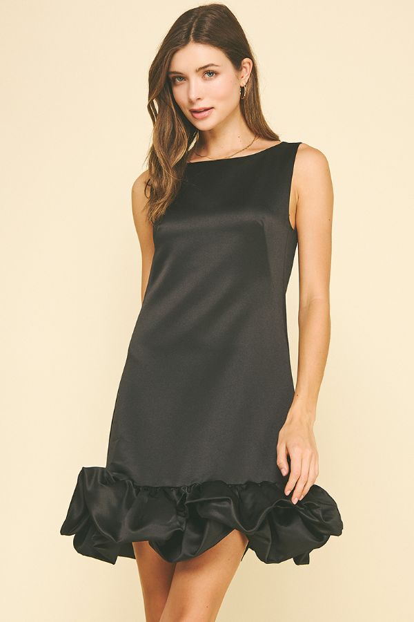 Woman wearing a black dress with ruffled hem on a beige background