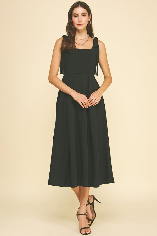 Woman wearing a black sleeveless dress against a beige background