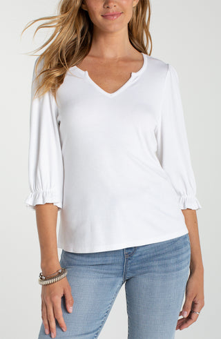 Woman wearing a white blouse with ruffled sleeves and light blue jeans on a plain background